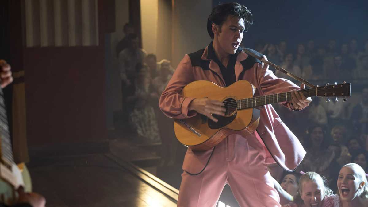 Austin Butler como Elvis Presley, vestido con un traje rosa y sosteniendo una guitarra.