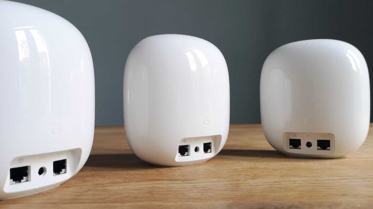 Tres dispositivos Google Nest WiFi Pro sobre una mesa, sus puertos Ethernet y tomas de corriente mirando hacia adelante.
